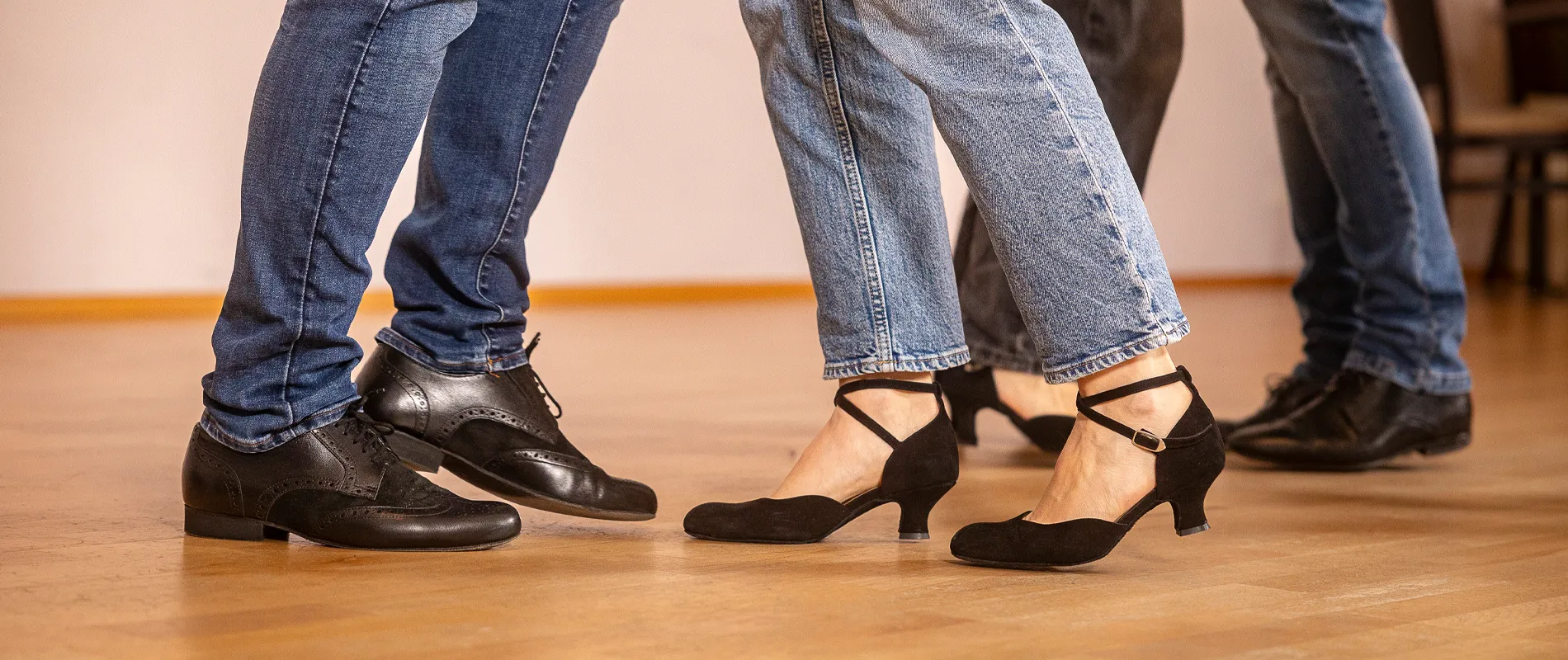 Tanzpaare beim gemeinsamen Tanzkurs auf einem Parkettboden in der Tanzwelt Regensburg – elegante Tanzschuhe und dynamische Schritte im Vordergrund.